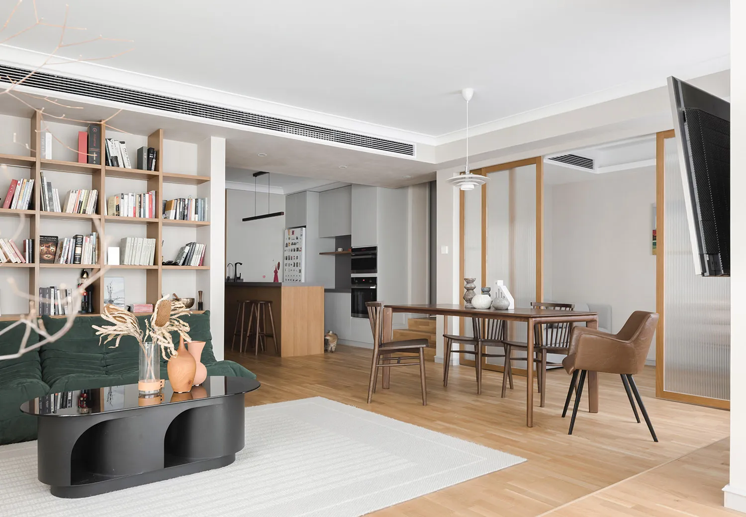 Modern living room with wood flooring, minimalistic furniture, and a large bookshelf.