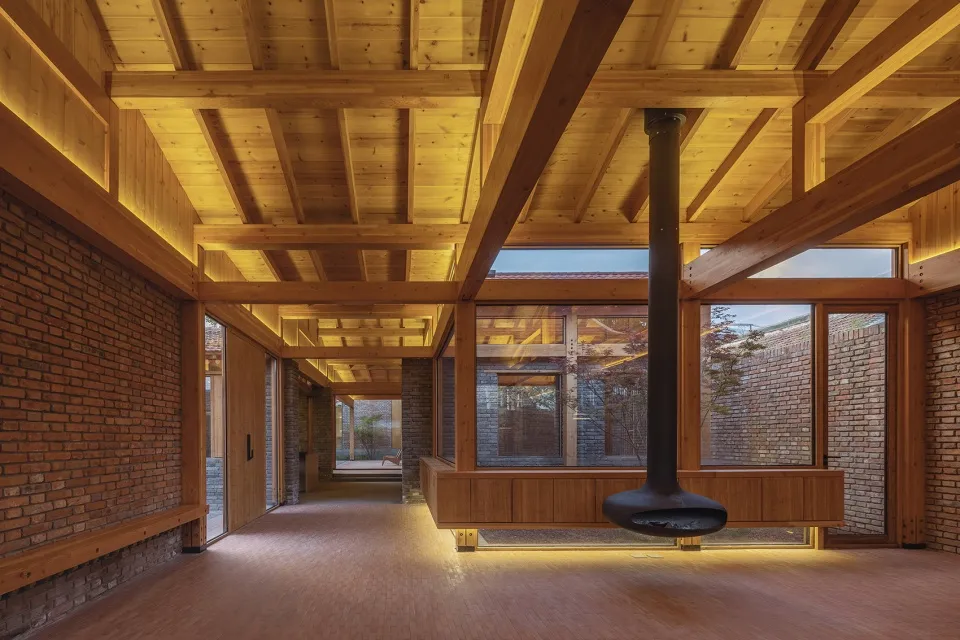 Modern living room with wooden ceiling beams, large windows, and a central fireplace.