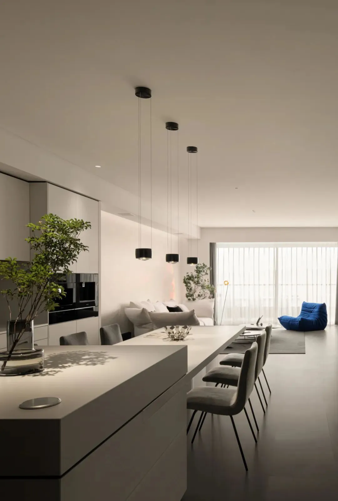 Modern minimalist living room and dining area with white concrete floor, minimalist furniture, and white cabinets.