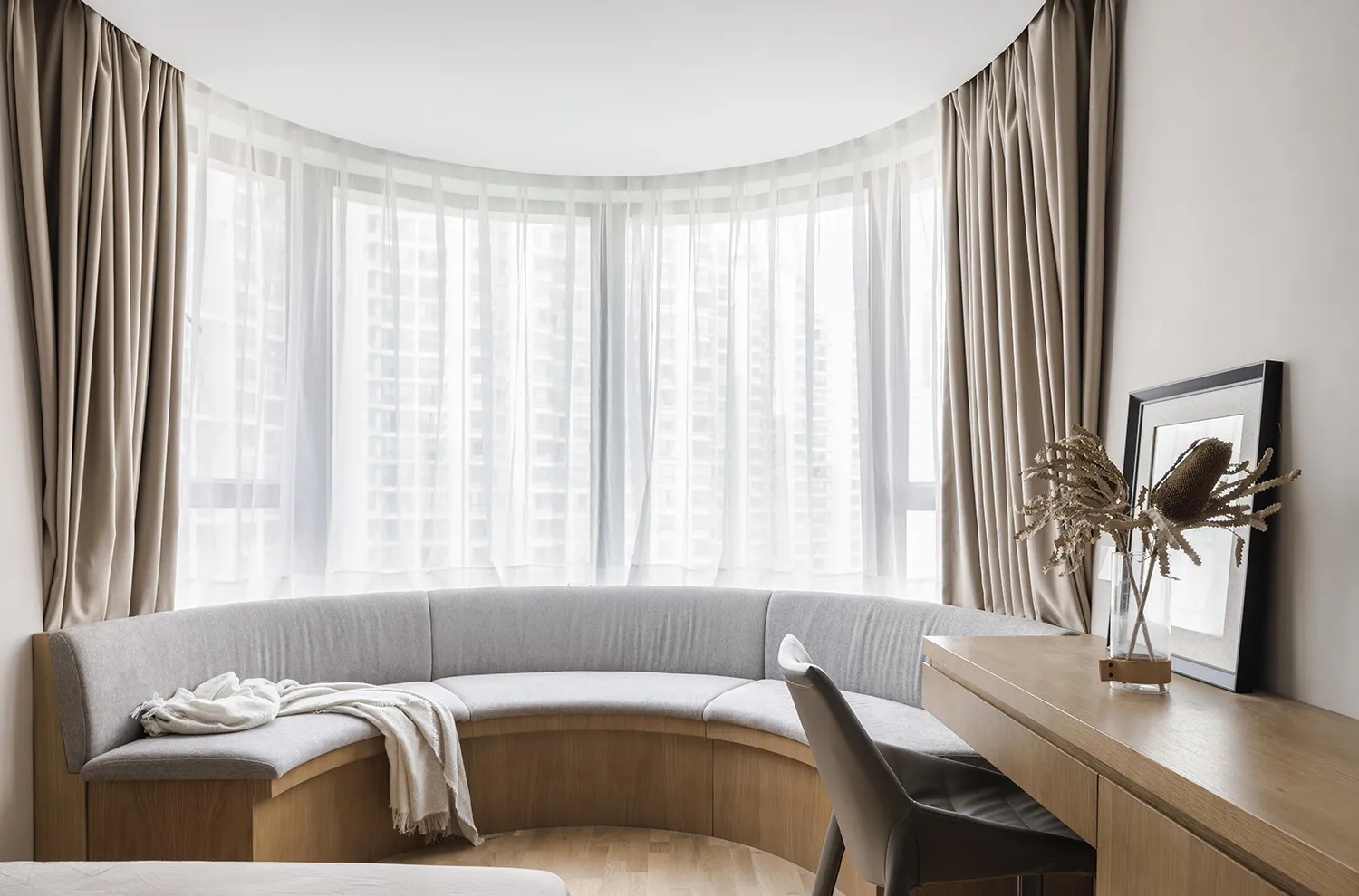 A modern living room with a curved bench seat upholstered in fabric and a wooden desk with a chair.