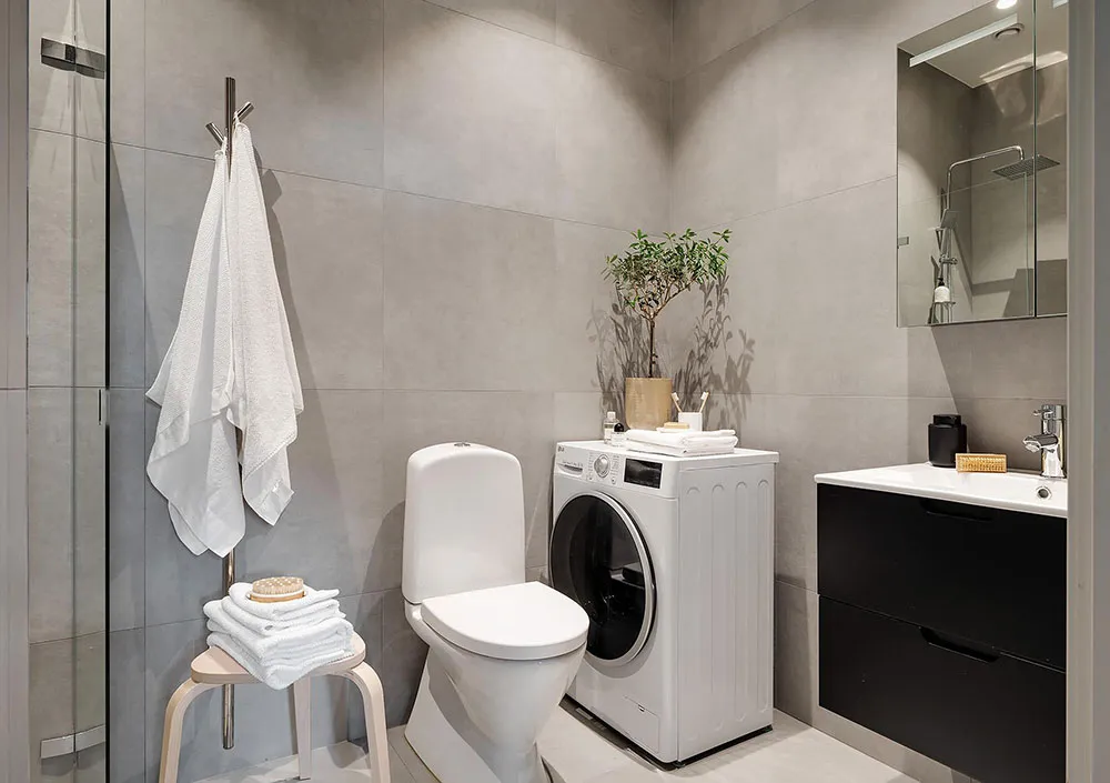 Modern minimalist bathroom with concrete walls, white toilet, white washing machine, black sink cabinet, and white towels.