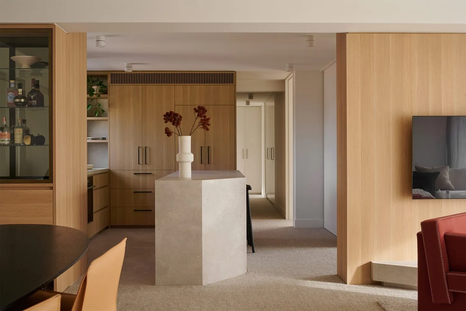 A modern residential interior featuring wooden cabinets and a marble column with a vase of flowers.