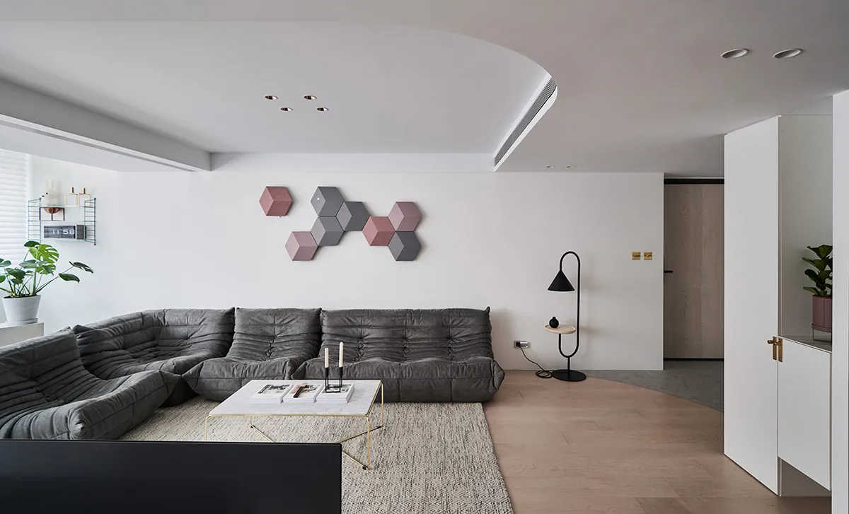 A modern living room featuring a gray sofa, minimalist decor, and a hexagonal art piece on the wall.