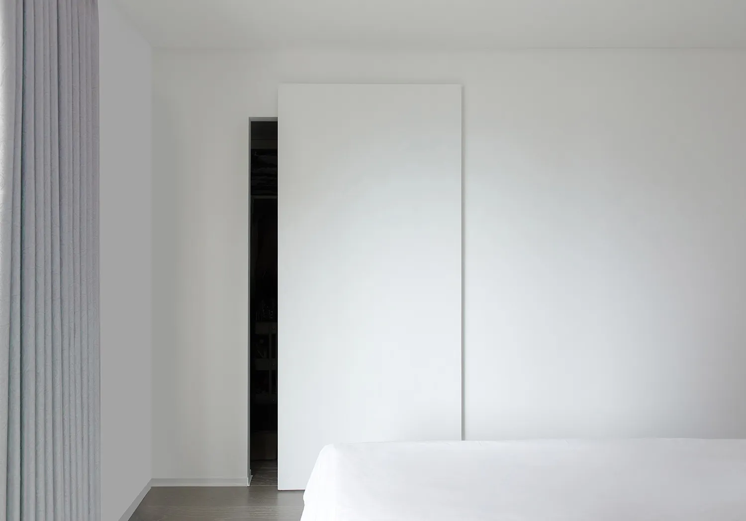 A minimalist bedroom with a white wall, bed, and sliding door.