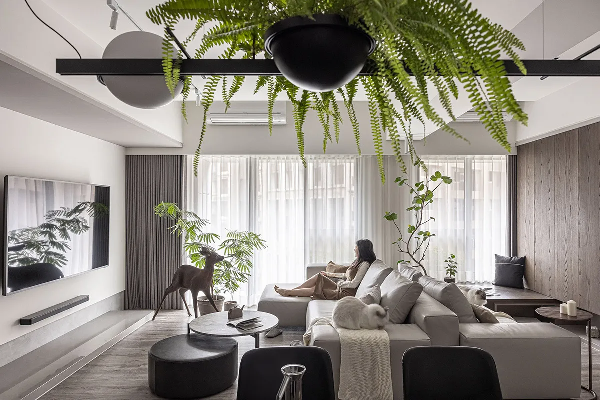 Modern, minimalist living room with concrete elements, plants, and a woman relaxing on a sofa.