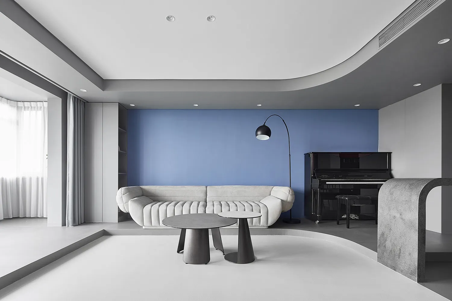 Modern living room with white furniture, blue accent wall, and black and white coffee tables.