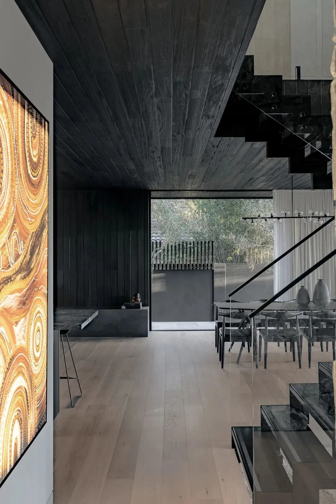 A modern living room with wooden flooring, glass railings, and a large window showcasing greenery outside.