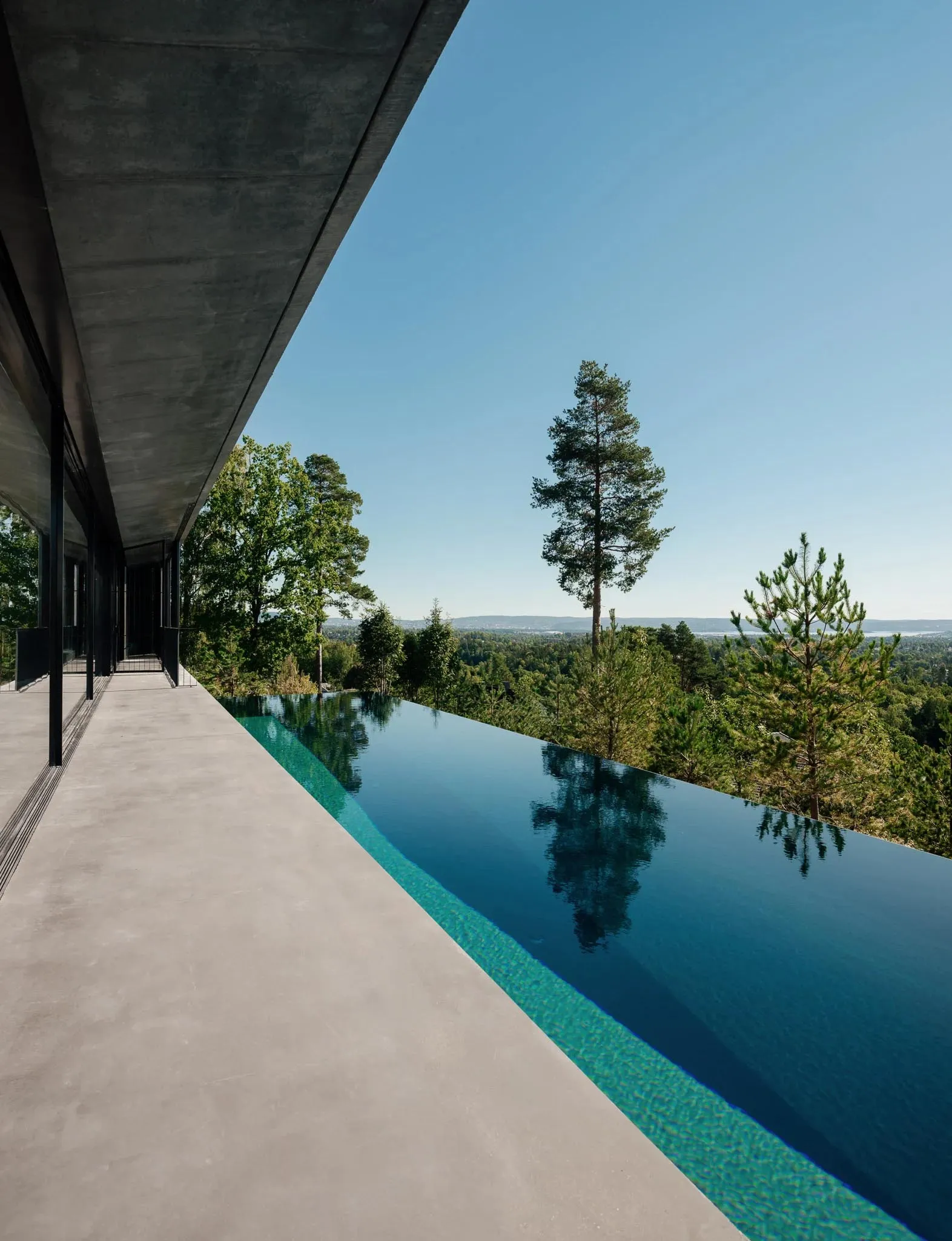 Modern luxury house with a concrete swimming pool overlooking a scenic landscape.