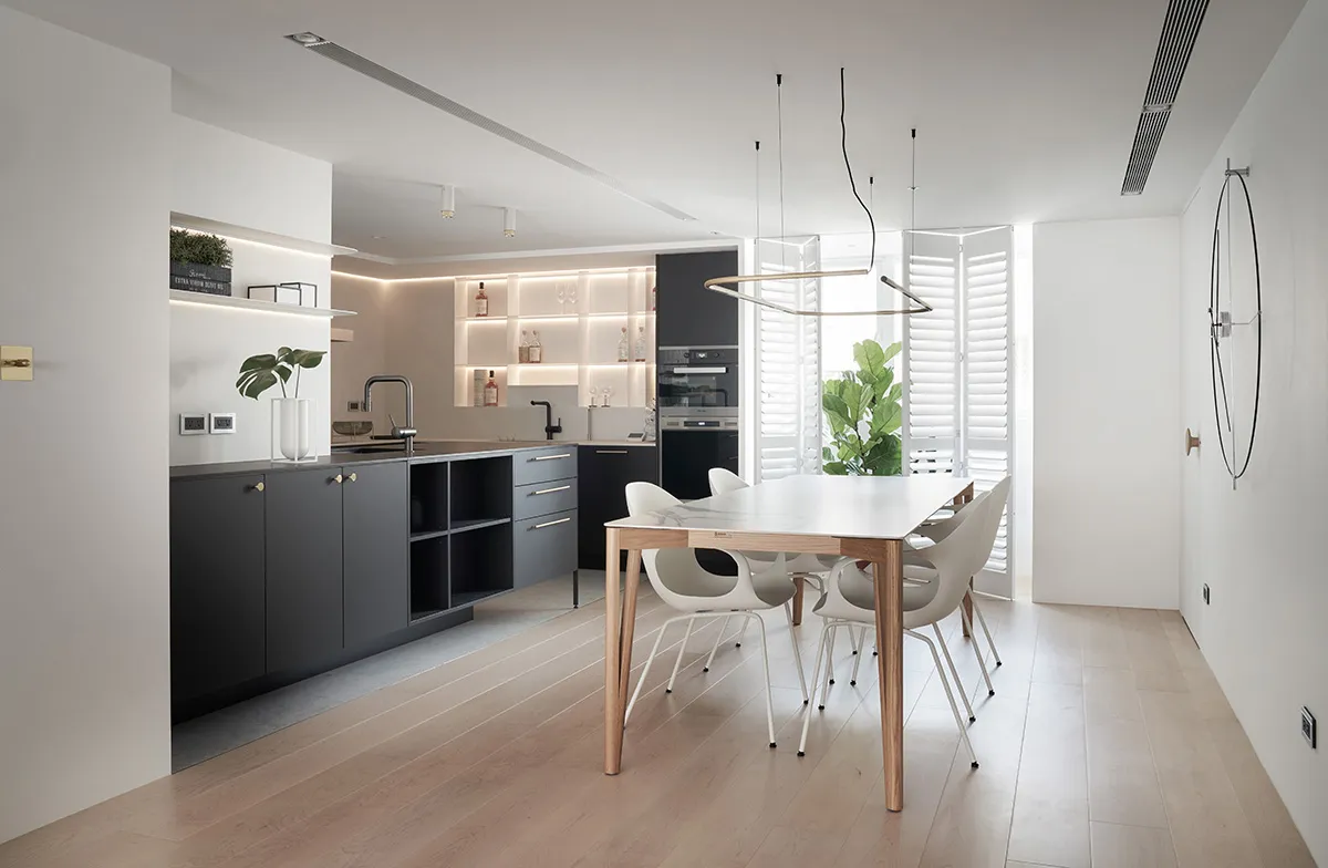 A modern, minimalist kitchen with black cabinets, white marble countertops, and a white dining table with white chairs.