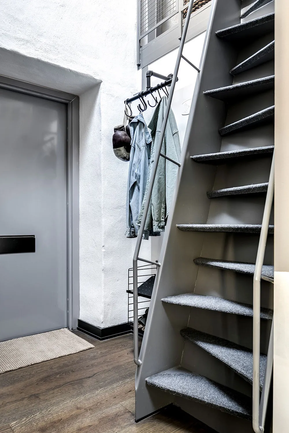 Modern staircase with a steel frame and gray carpet tiles leading to a door with a metal handle.