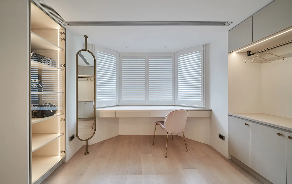 A minimalist wardrobe room featuring wood, glass, and metal materials, with a large mirror and a comfortable seating area und