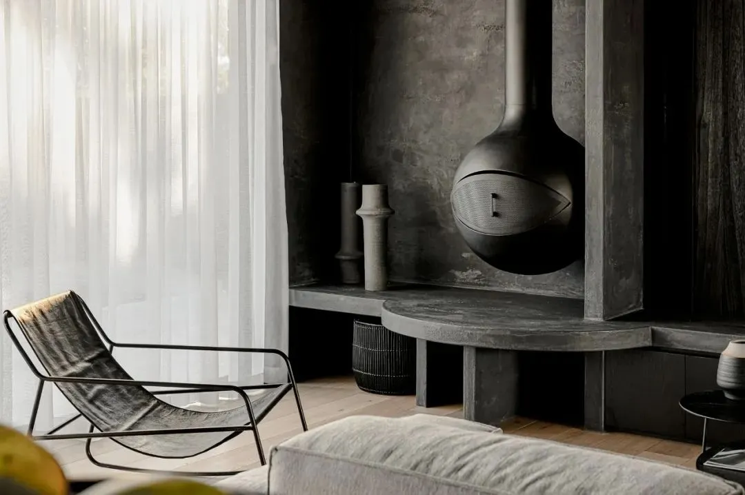 A modern minimalist living room featuring a concrete fireplace and a lounge chair in front of a large window with sheer white