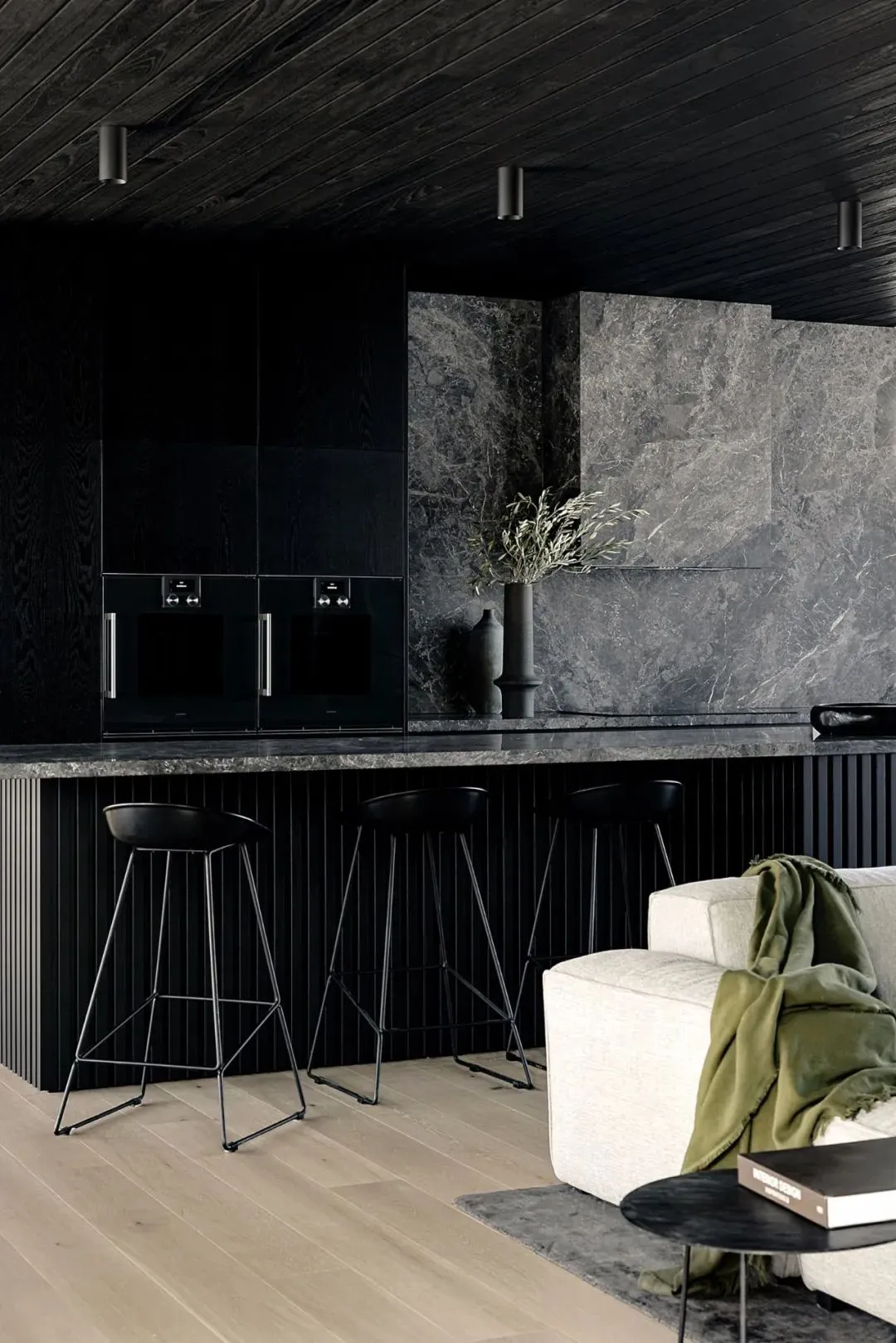 A minimalist residential kitchen showcasing a marble countertop and backsplash, with black stools and sleek black cabinetry.