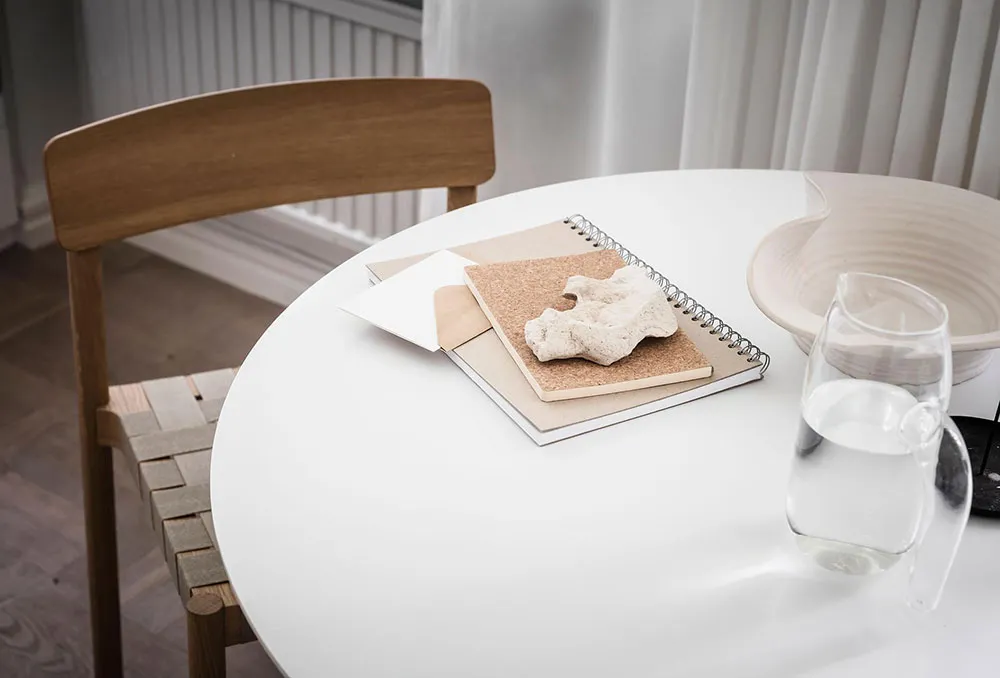 A simple minimalist interior design featuring wooden chairs, a paper notepad, and a glass pitcher with water.