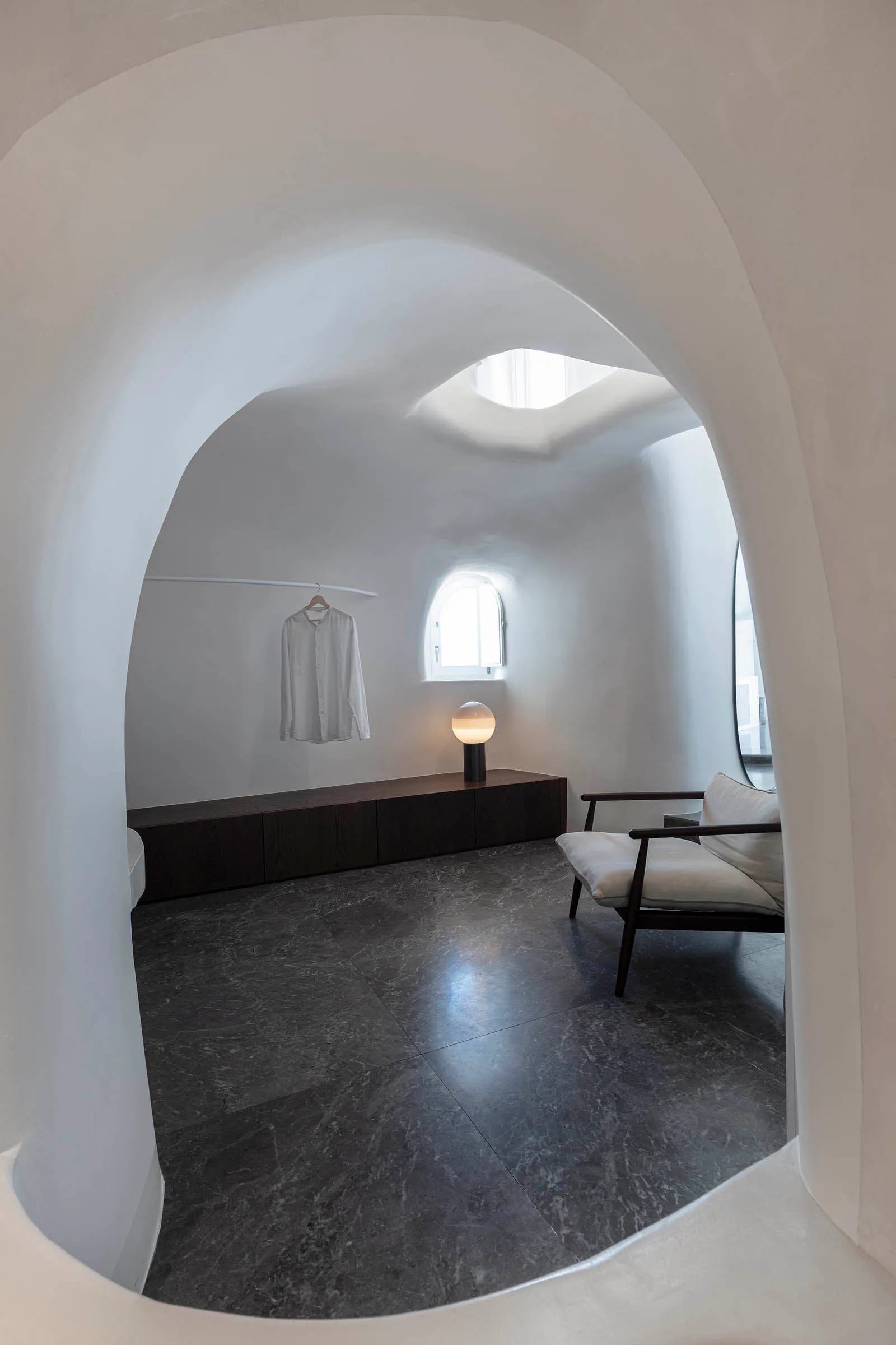 A modern, minimalist residential interior with white cement walls, dark marble floor, and a minimalist seating area with a wh