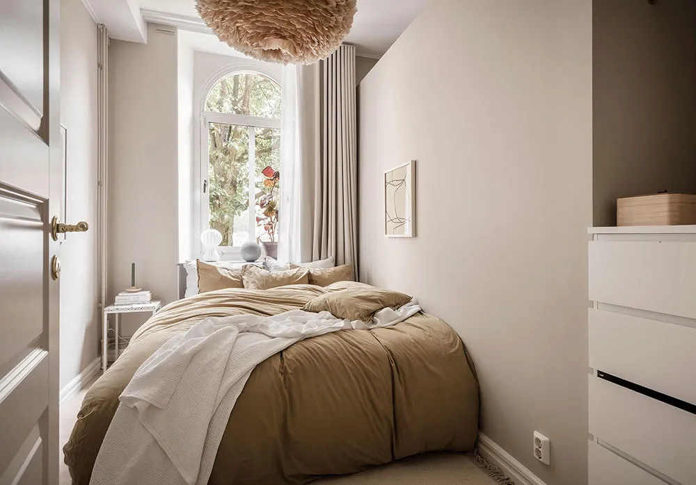 A minimalist bedroom with a bed covered in beige textiles and a floating light fixture above it.