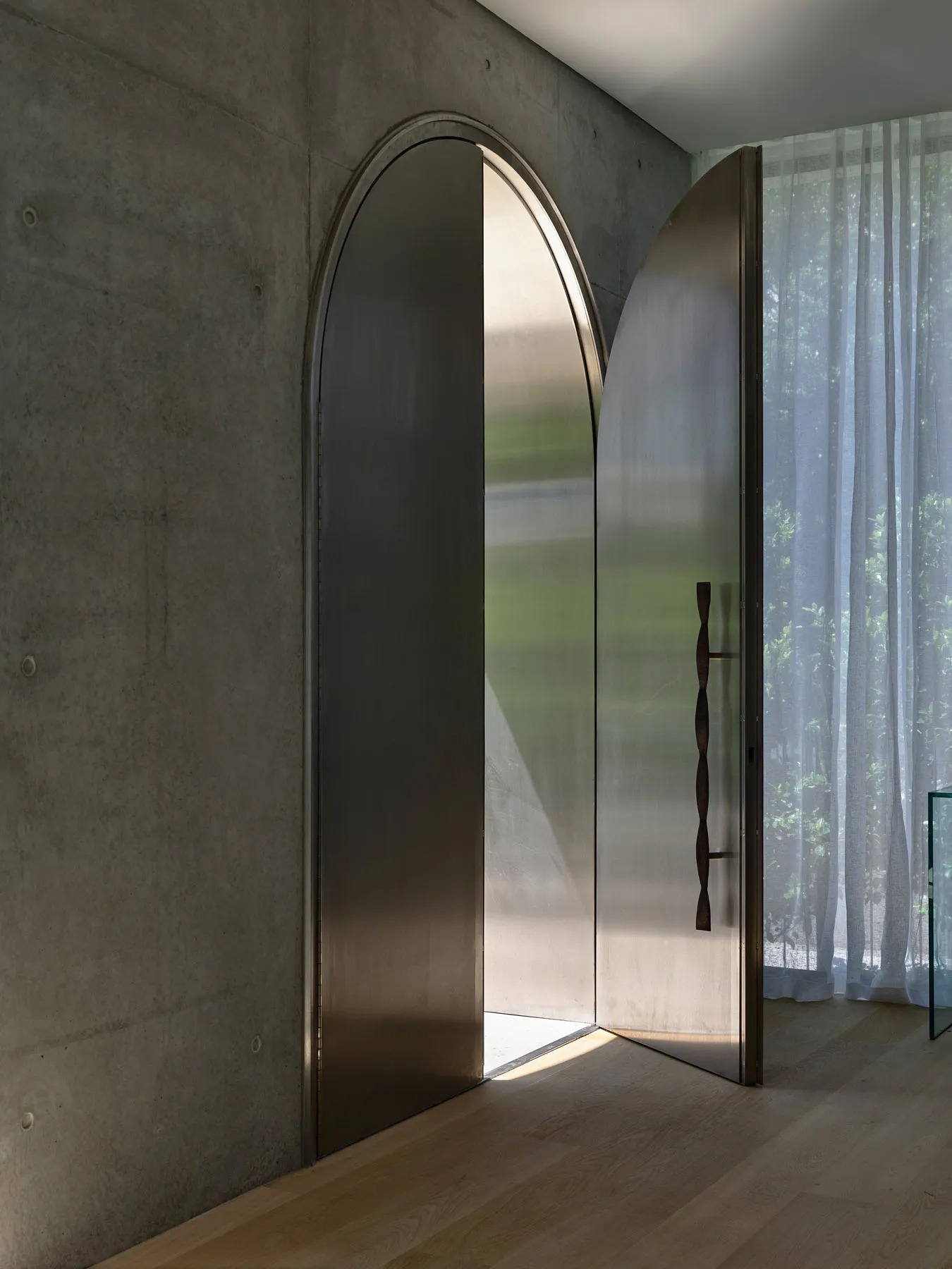 A minimalist entrance with an arched metal door in a modern interior design setting.