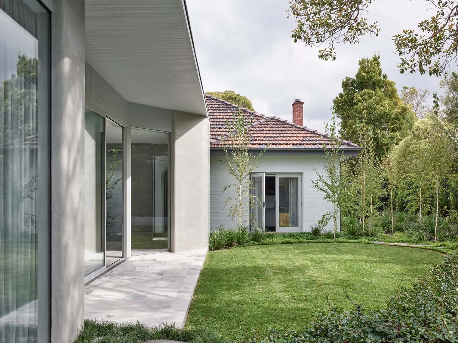 Modern-style exterior residential backyard with concrete patio and grass lawn, featuring a white house with a red roof and br