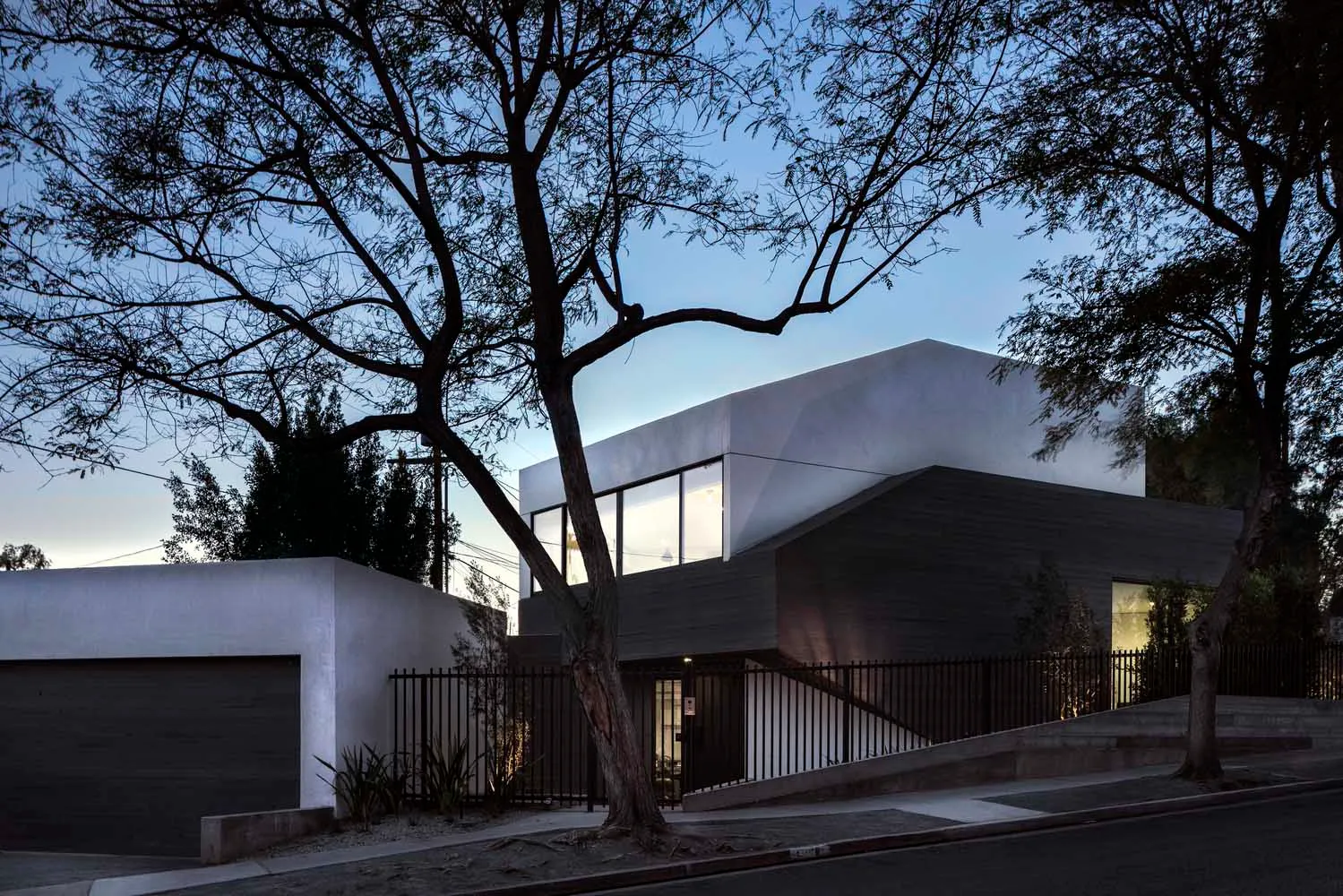 A modern concrete house with large windows and a black fence.