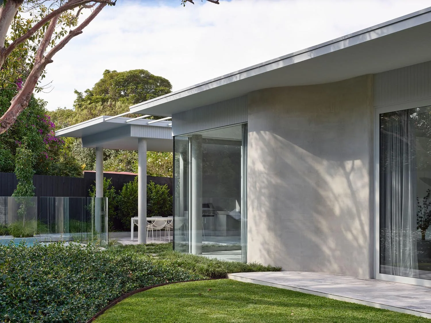 A modern house featuring a concrete exterior with large glass windows and a spacious garden.