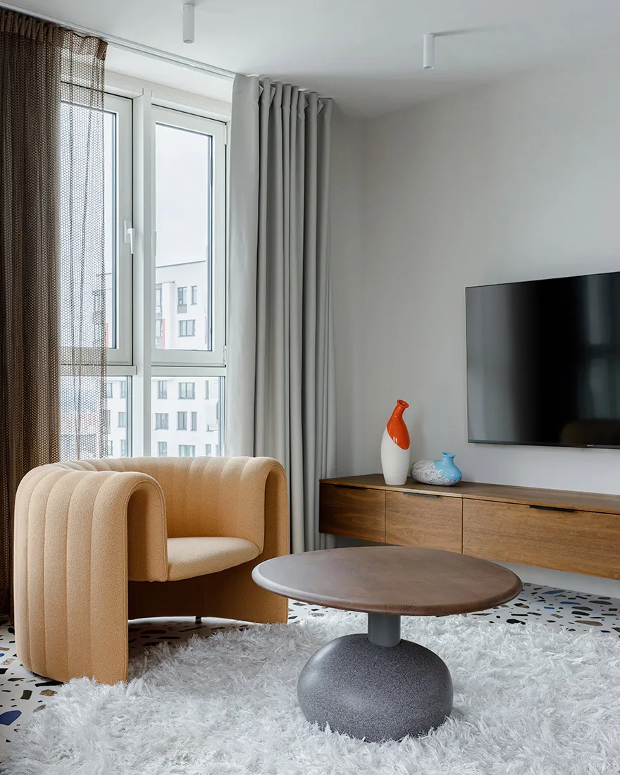 A minimalist living room featuring a fabric armchair, wooden table and terrazzo flooring.