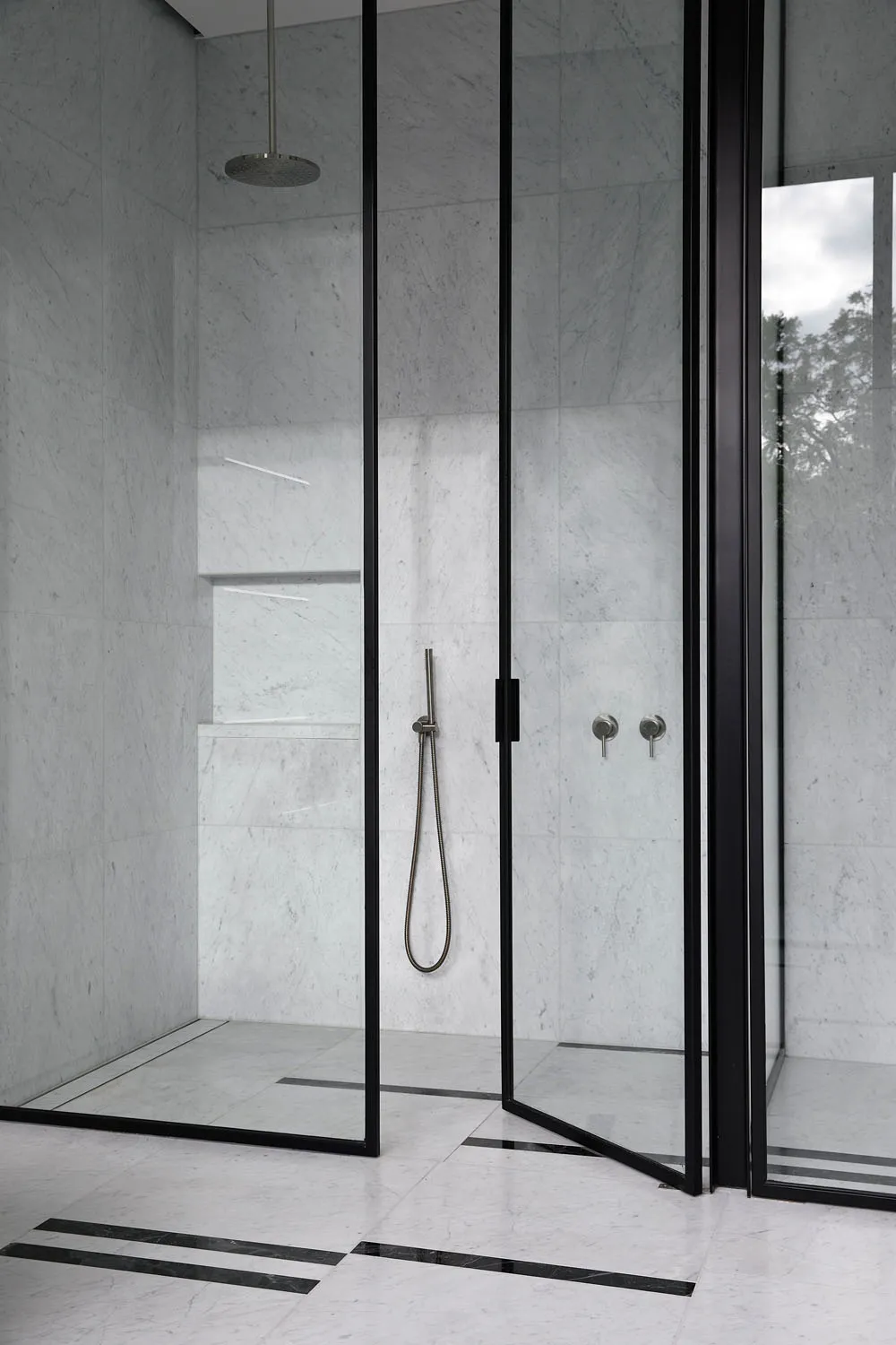 A minimalist bathroom with white marble walls and black fixtures.
