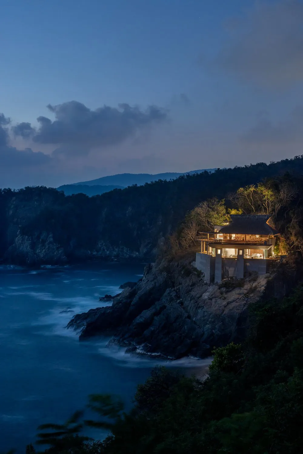 A modern residential house built on a rocky cliffside with concrete walls and wooden accents.