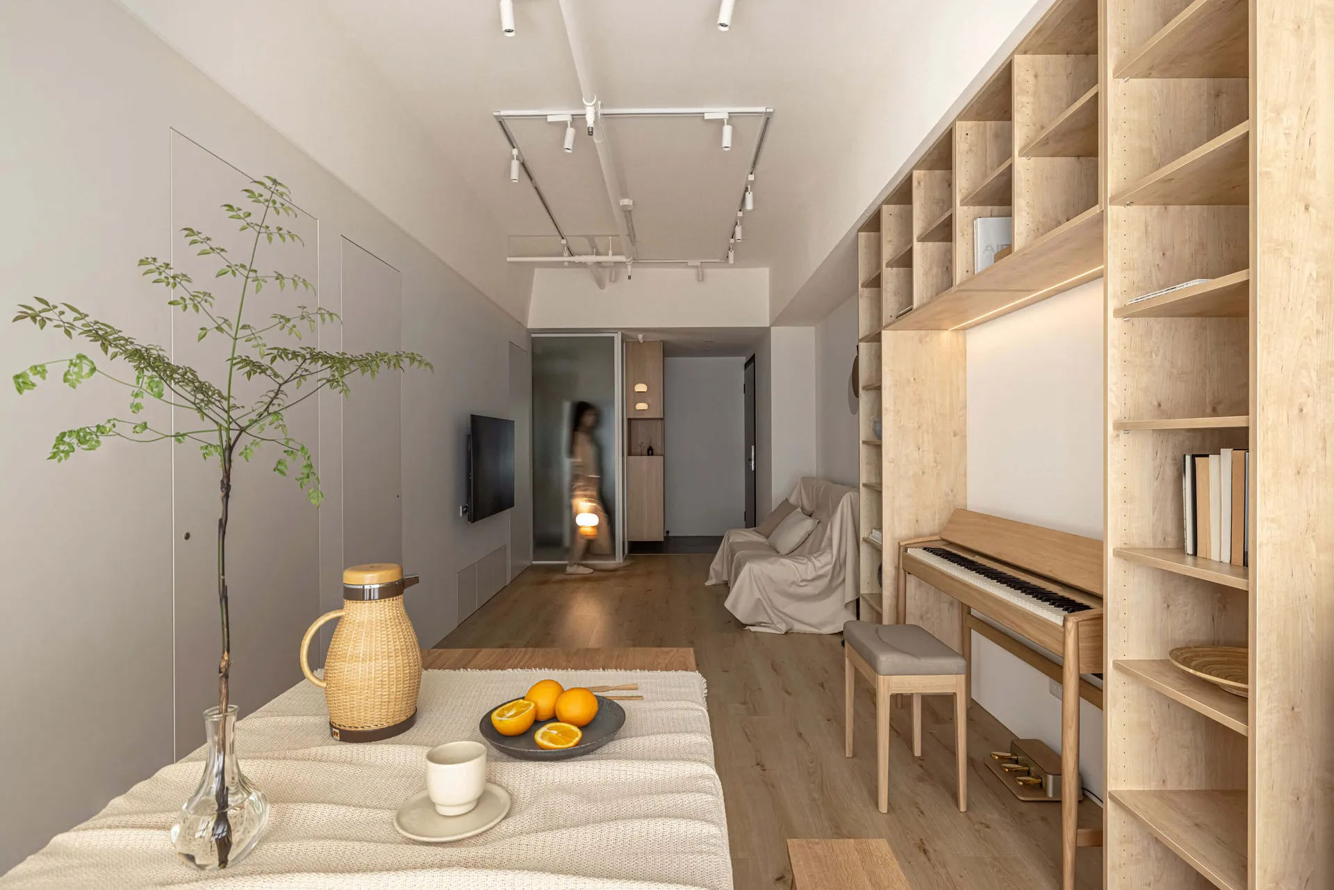 A minimalist living room with wooden shelves, a piano, and an orange on a plate.