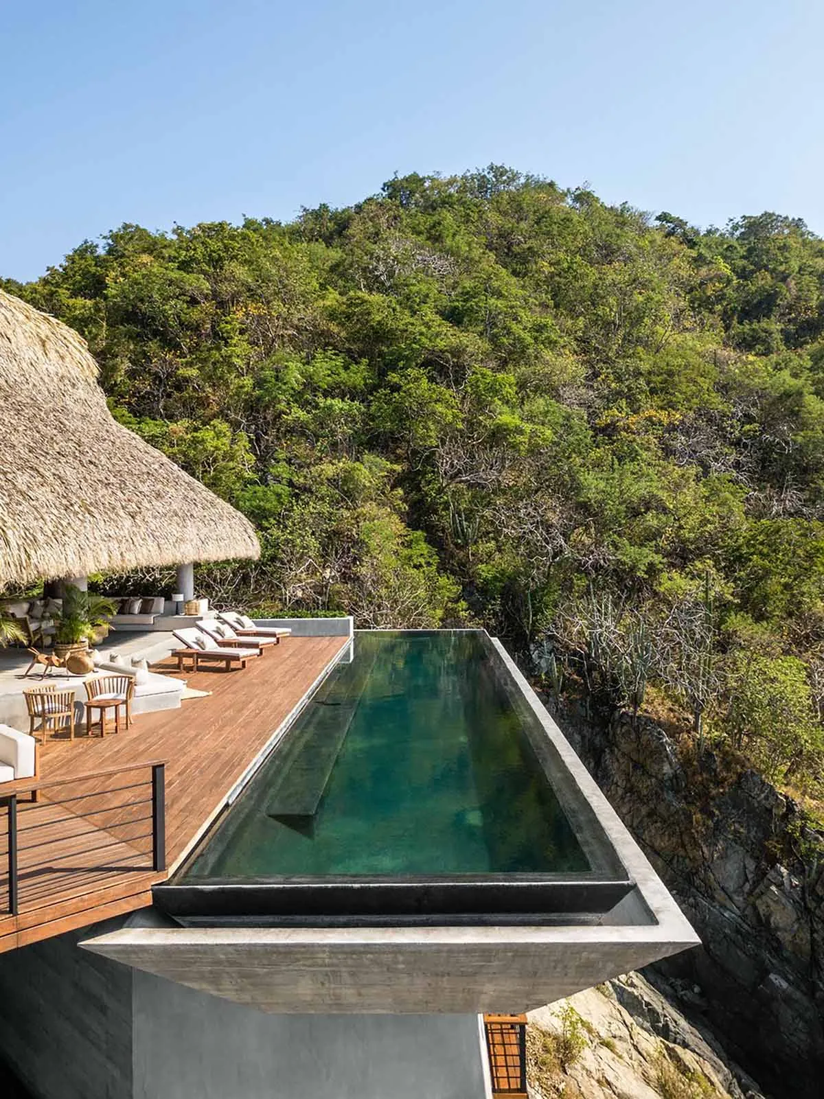 Modern concrete swimming pool overlooking dense green hillside
