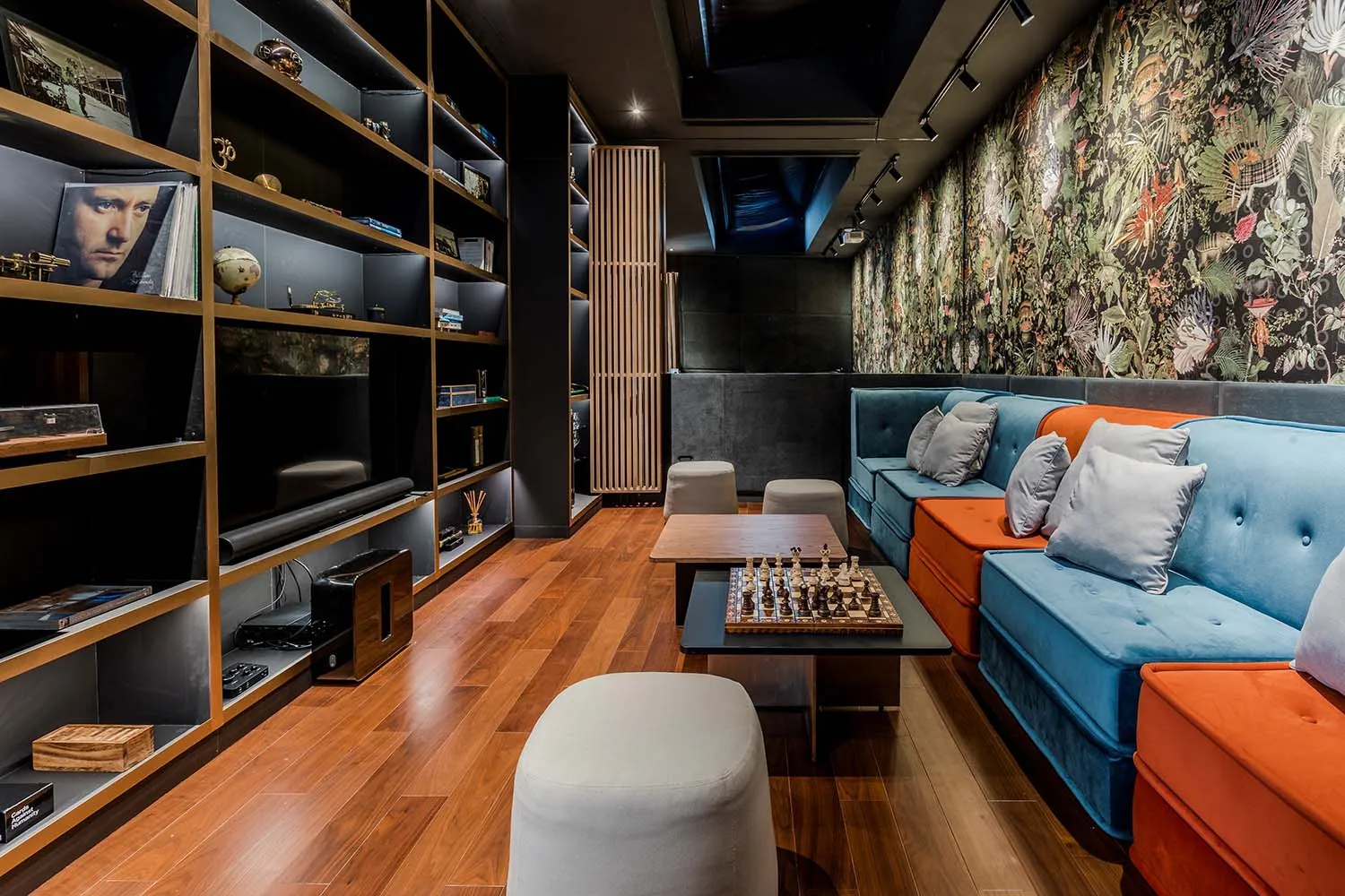 Modern industrial living room with blue and orange sofas, wooden floor, and bookshelves.