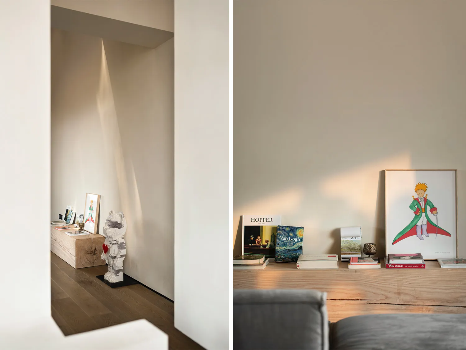 A modern living room with white walls and wooden furniture, featuring books, a sculpture, and artwork.