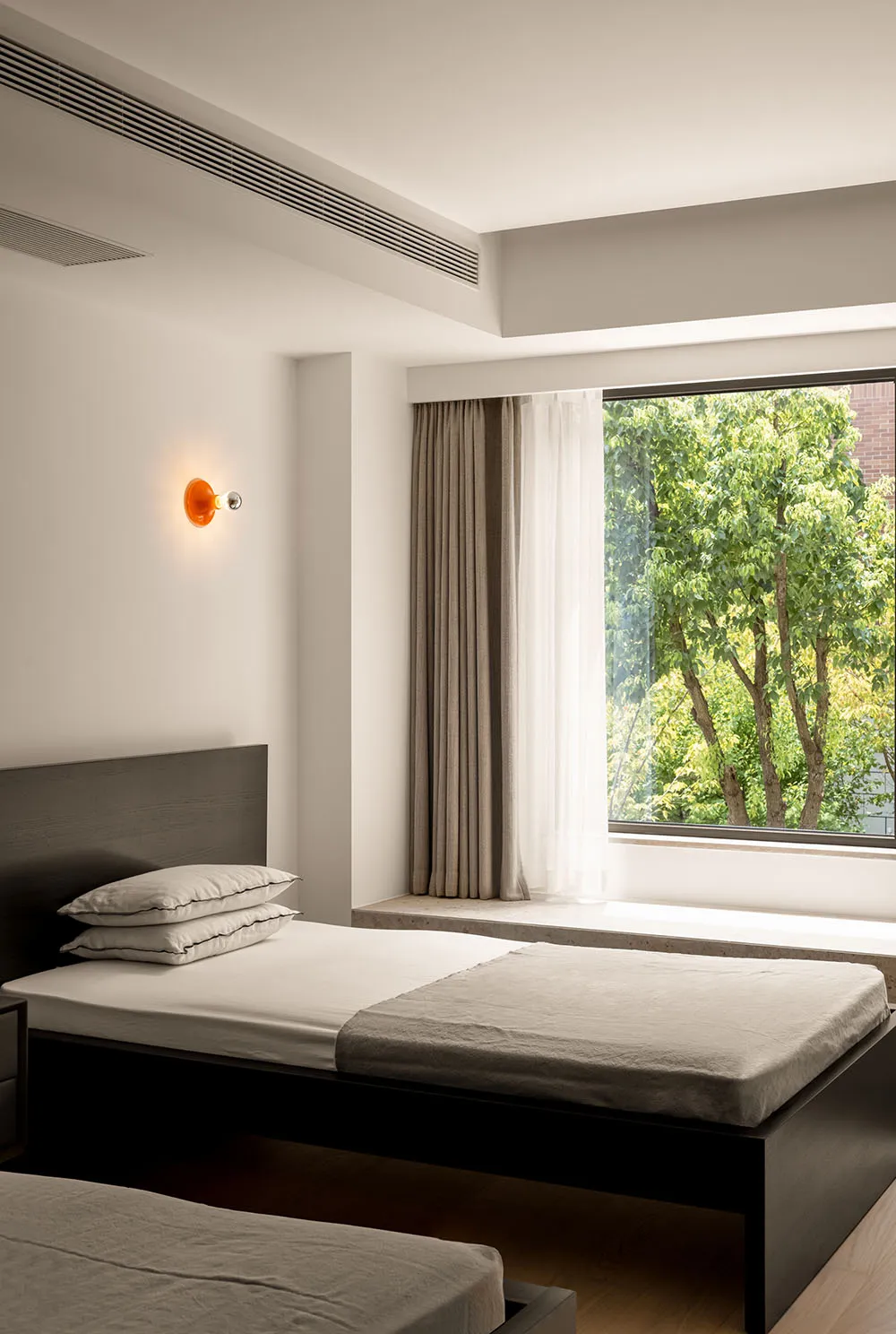 A modern minimalist bedroom with a bed, fabric curtains, and a large window with a view of trees.