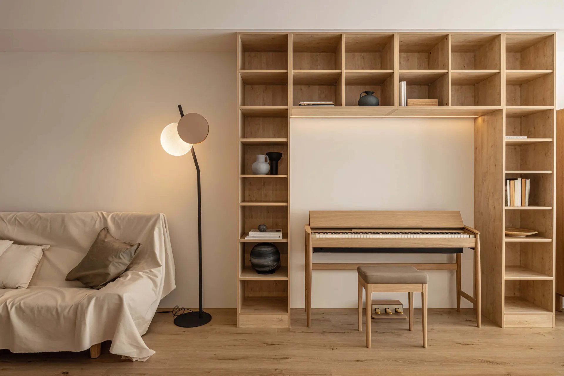 A minimalist living room with wooden shelves and a piano, featuring a sofa and floor lamp.