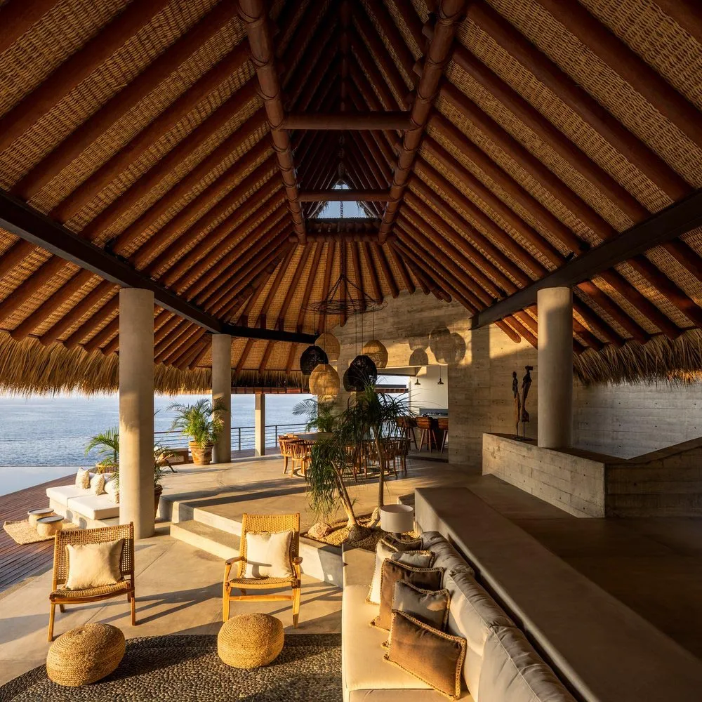 A modern living room with wooden beams on the ceiling and walls, natural light, and comfortable furnishings.