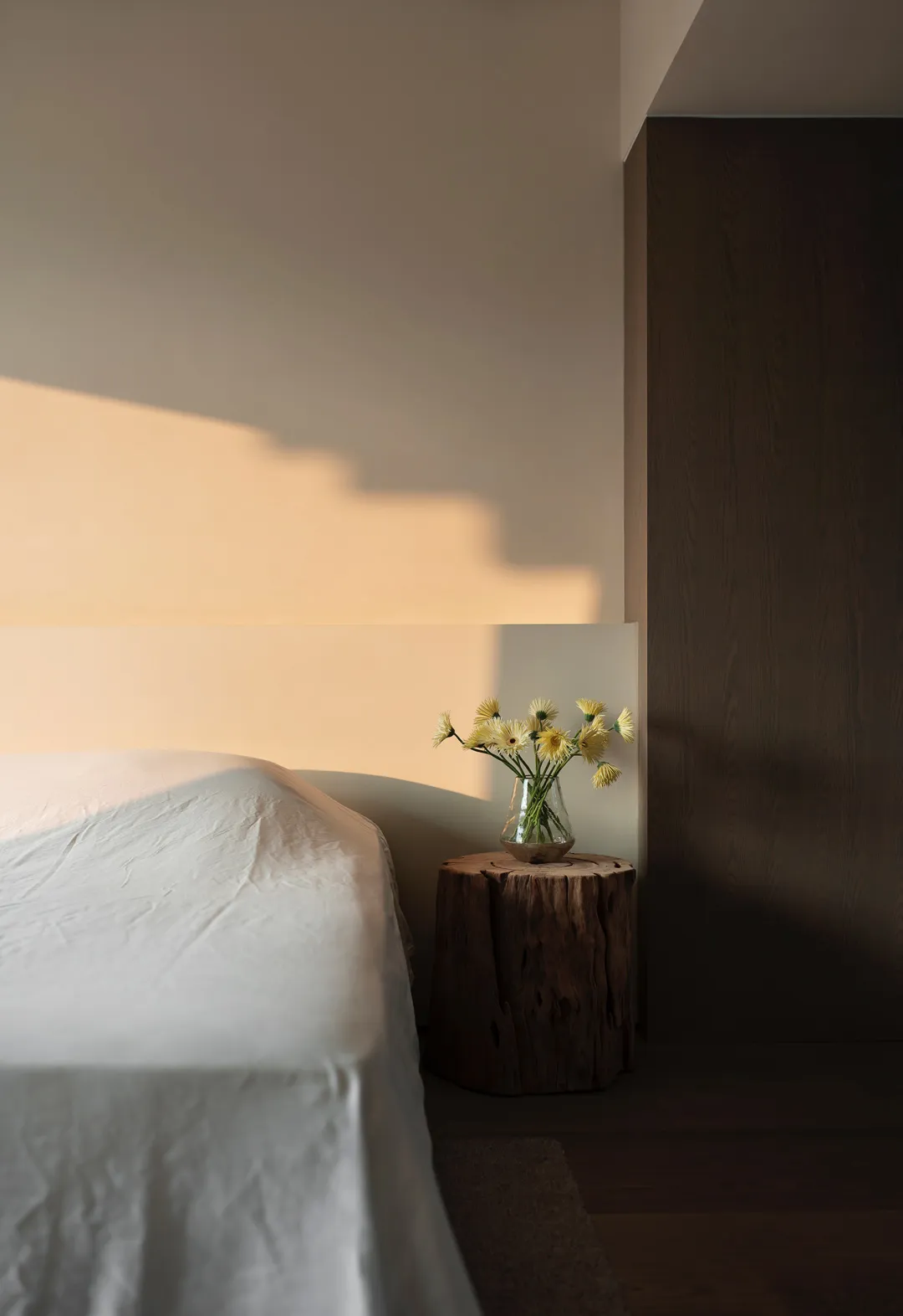 A minimalist bedroom featuring a wooden log nightstand with a vase of flowers.