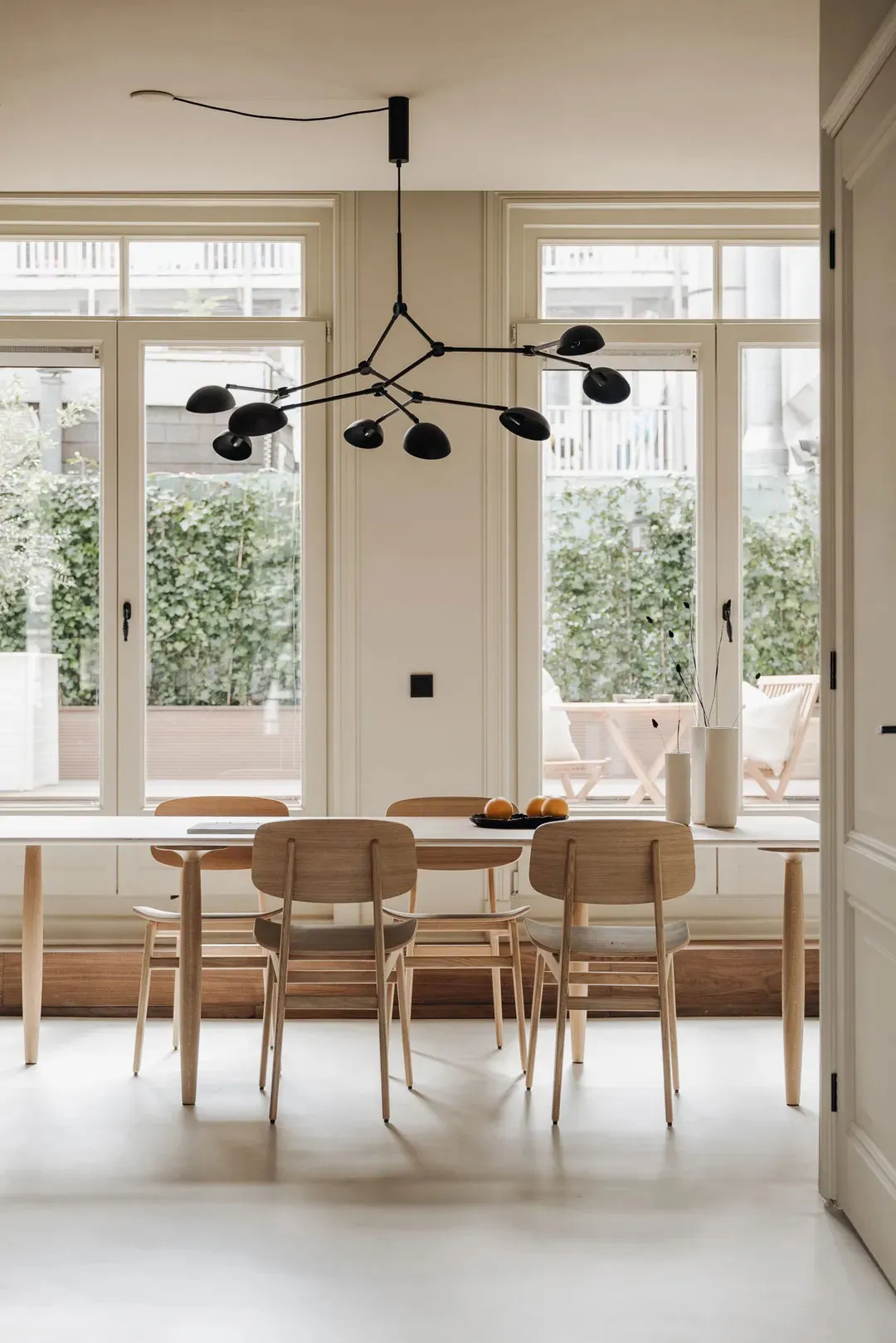 A minimalist dining room with wooden furniture, large windows, and a modern chandelier hanging above the table.