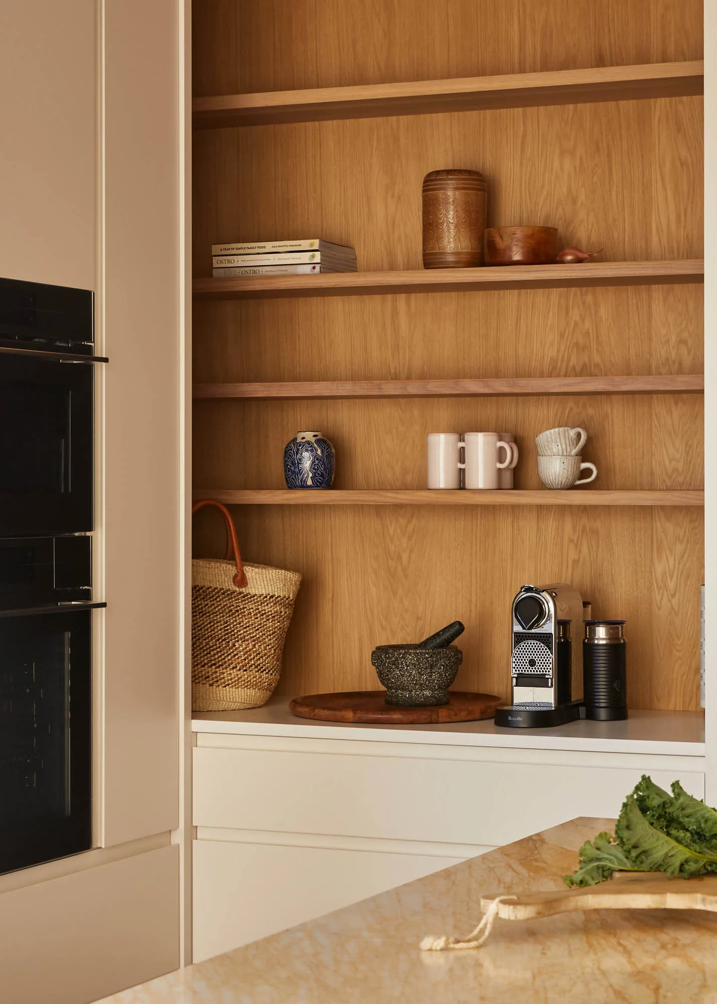 A minimalist kitchen with wooden shelves holding books, mugs, and a coffee machine. Interior design focus on storage solution