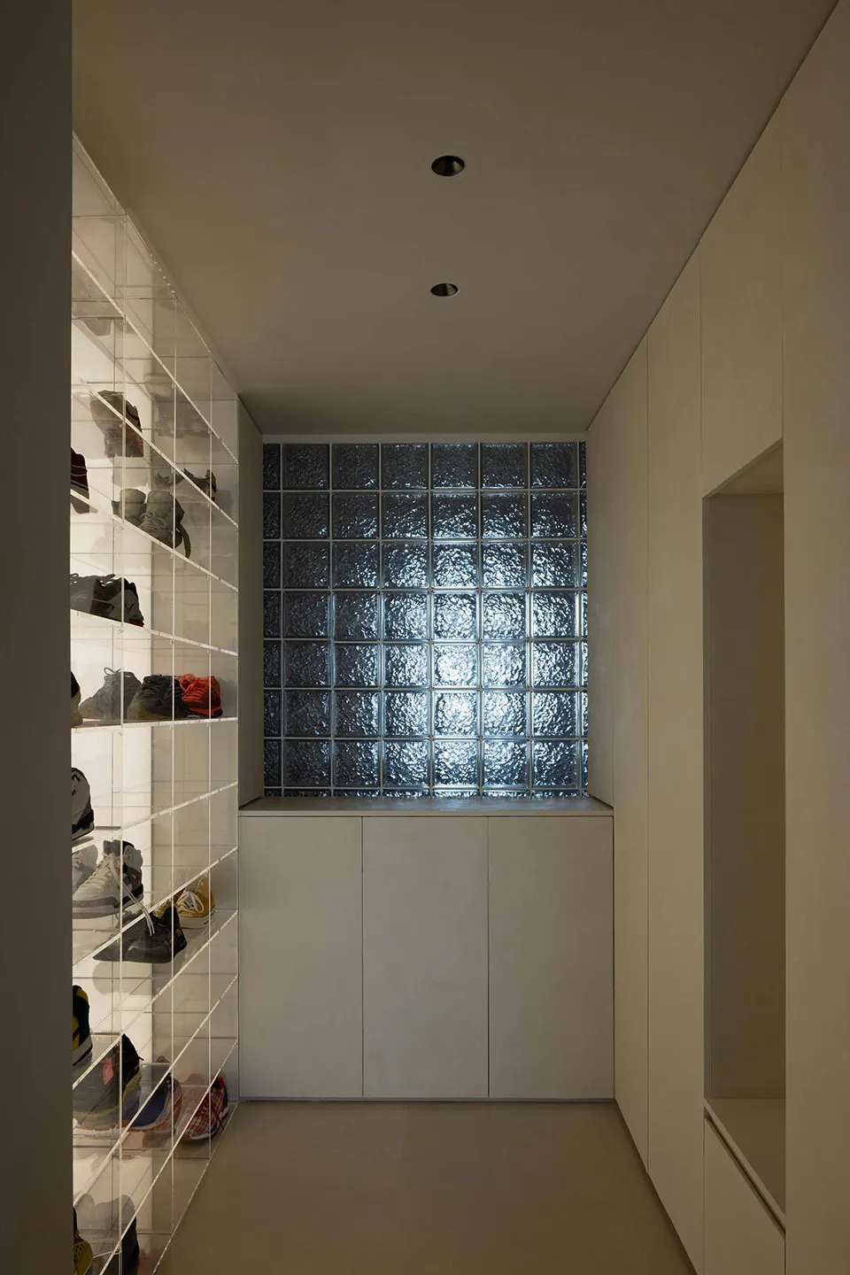 A minimalist shoe closet featuring a glass wall and storage units