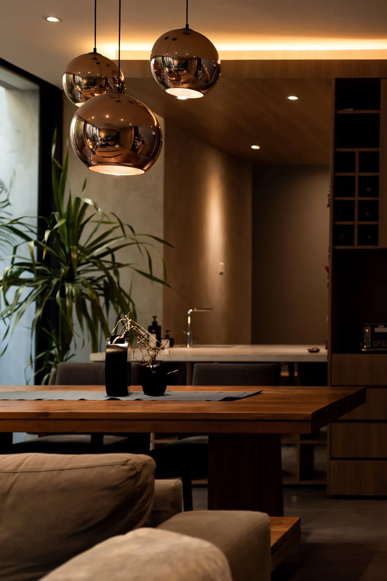 A modern minimalist dining room featuring a wooden table with a dark finish, minimalist pendant lights, and a sleek, contempo