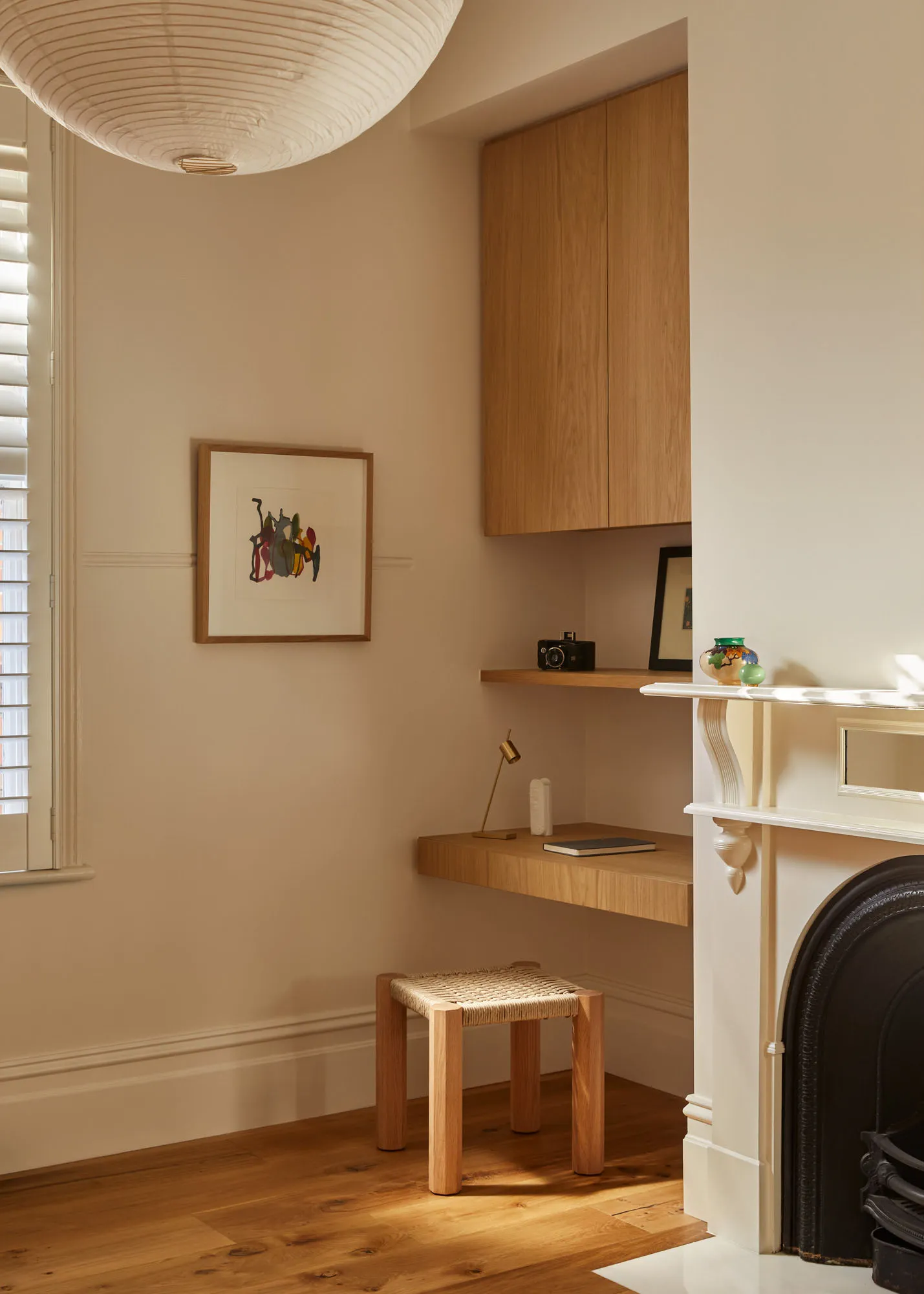 A minimalist home office featuring a wooden desk, shelves, and a stool under a pendant lamp, with a warm, cozy atmosphere.