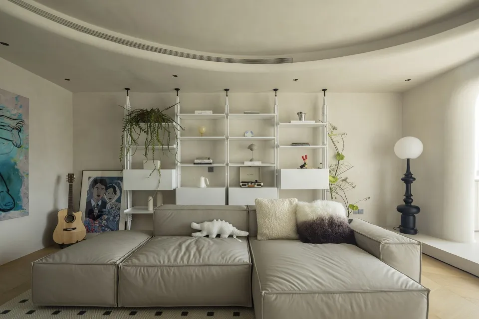 A minimalist living room featuring neutral-colored furnishings, a white bookshelf, and green plants.