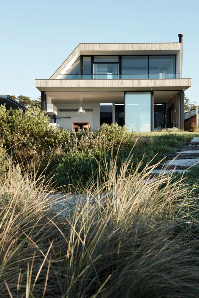 A modern house with a concrete and glass exterior, featuring a sleek, two-story design with large windows and a minimalist ae