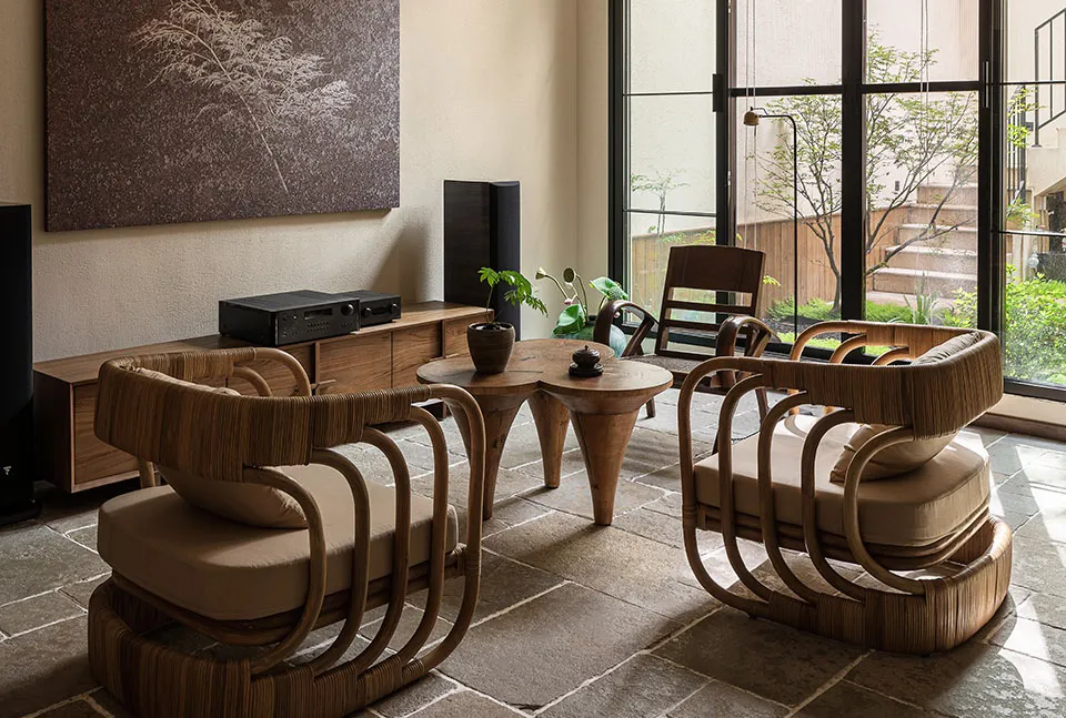 Modern living room with wooden and rattan furniture, plants, and a view of the outdoors.
