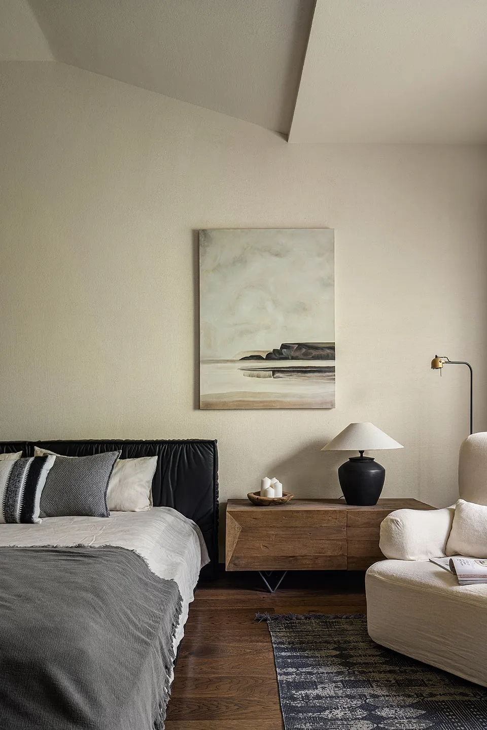 Modern, minimalist bedroom featuring a black upholstered bed and a wooden sideboard with a table lamp.