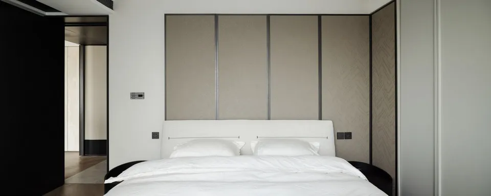 Modern minimalist bedroom with white bed, neutral-toned fabric wall panels, and black trim.
