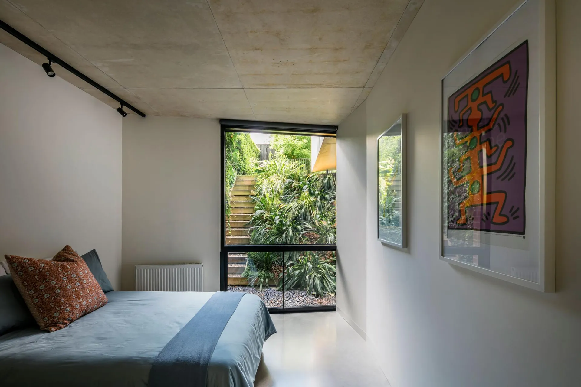 Minimalist bedroom with a window offering a view of greenery and stairs.