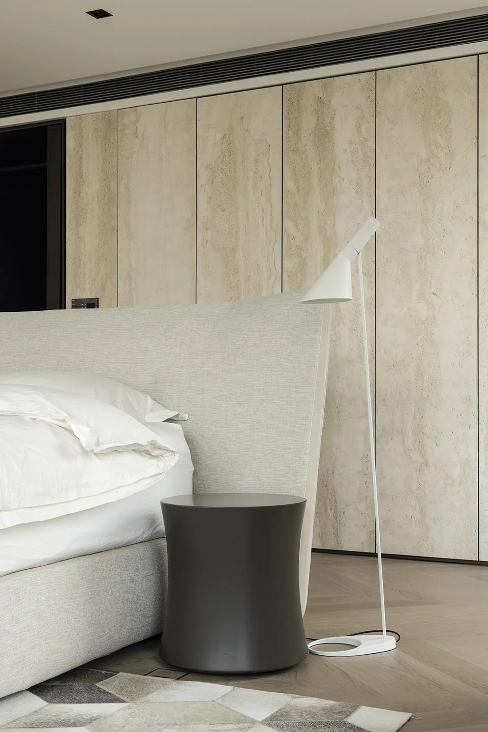 Minimalist bedroom featuring fabric bed, wooden cabinet, and metal lamp.