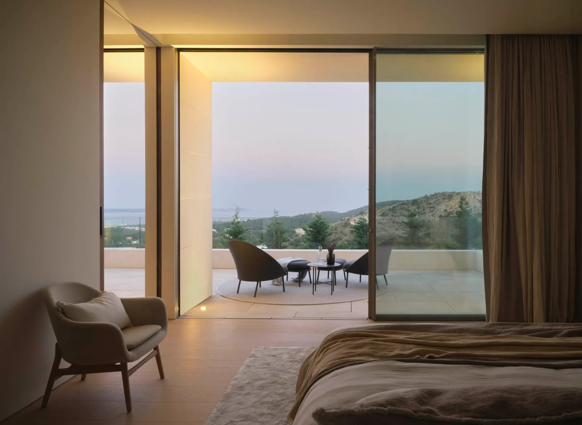 Modern bedroom with wooden flooring and glass walls overlooking scenic landscape.