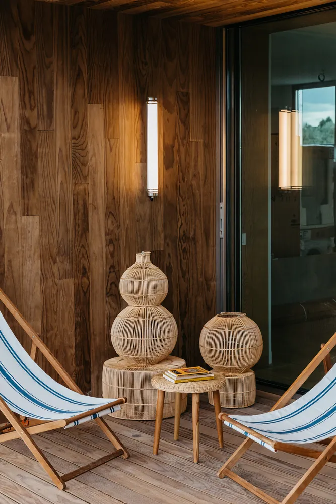 Modern wooden deck chairs and woven lanterns on a wooden floor.