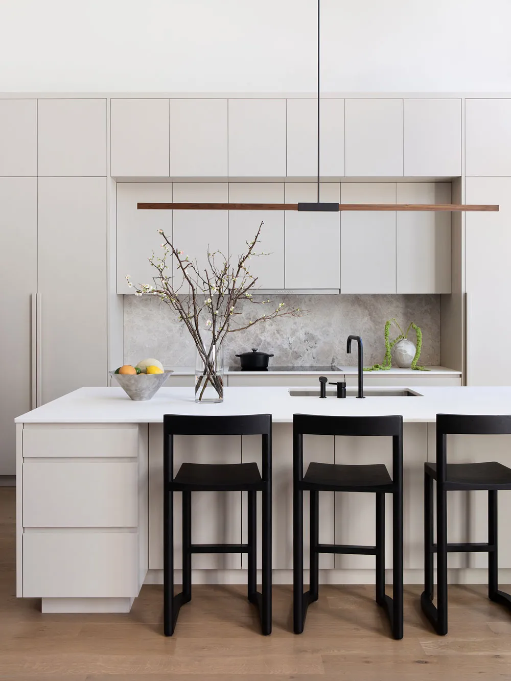 A minimalist kitchen with white cabinets, a white countertop, and black stools.